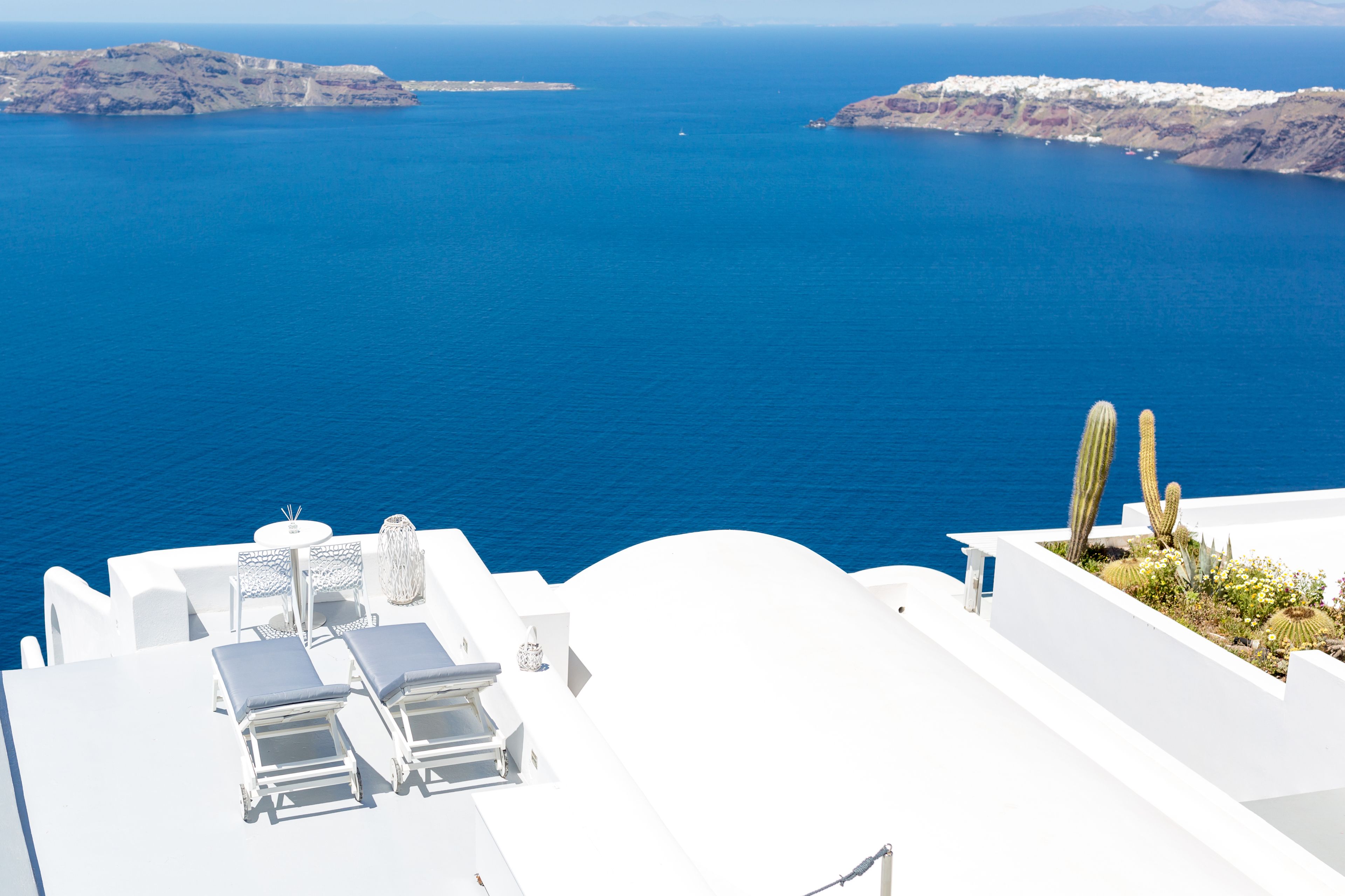 A white building with a pool and lounge chairs overlooking a blue sea.