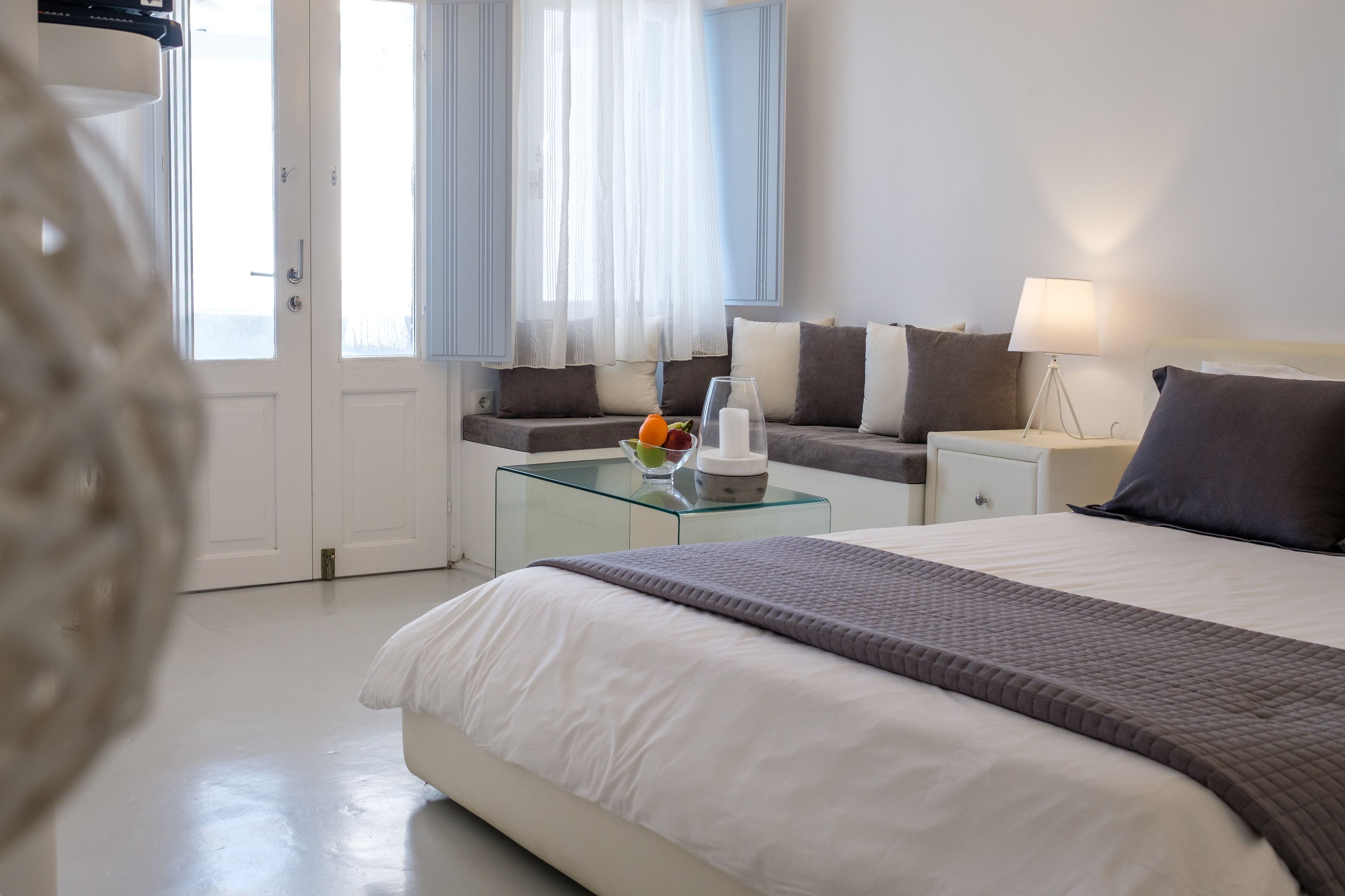 A modern hotel room with a large bed, a glass side table, a bedside table, and a view of the outdoors through a door.