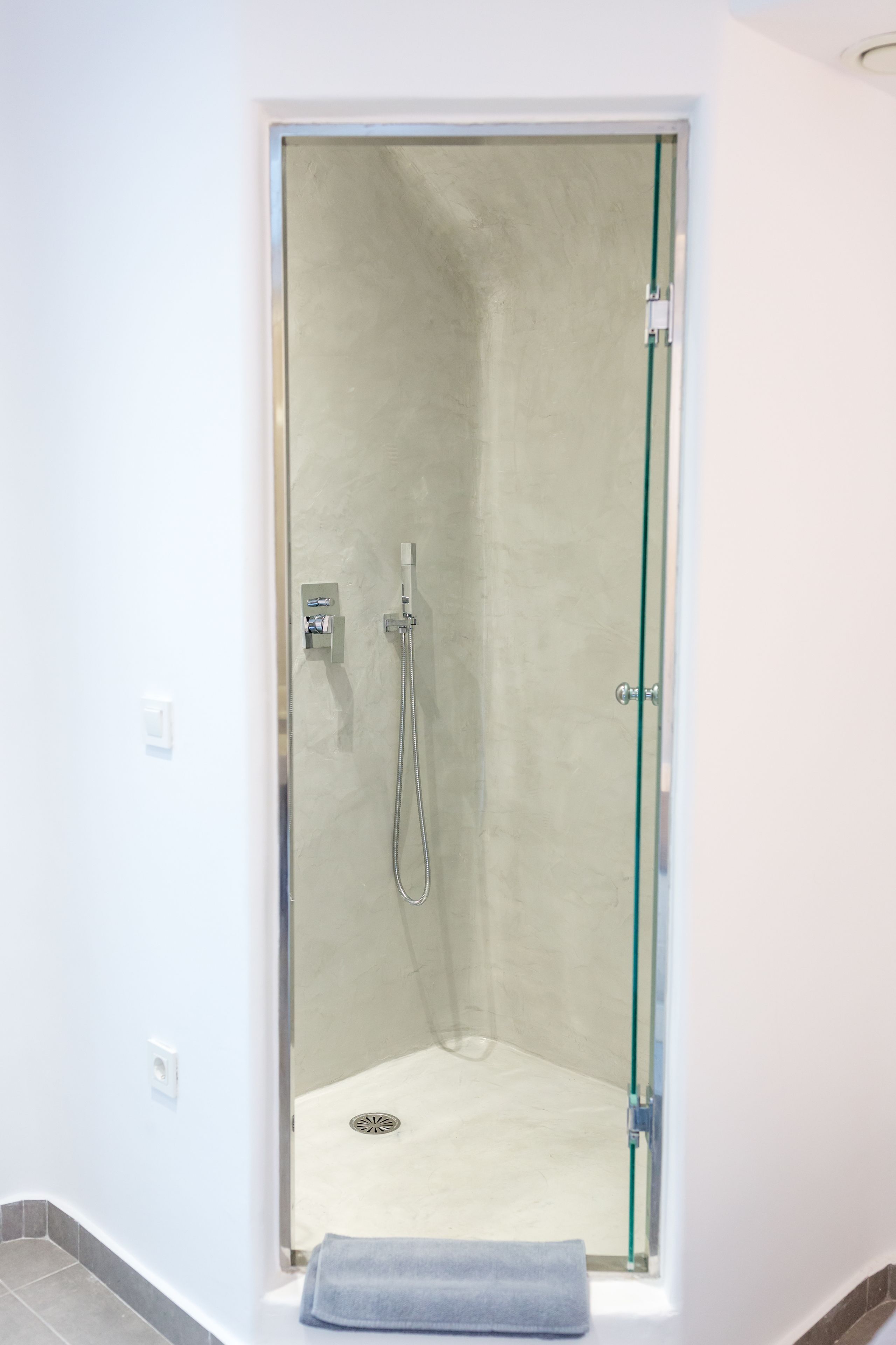 A glass-enclosed shower with a handheld showerhead and a wall-mounted faucet.
