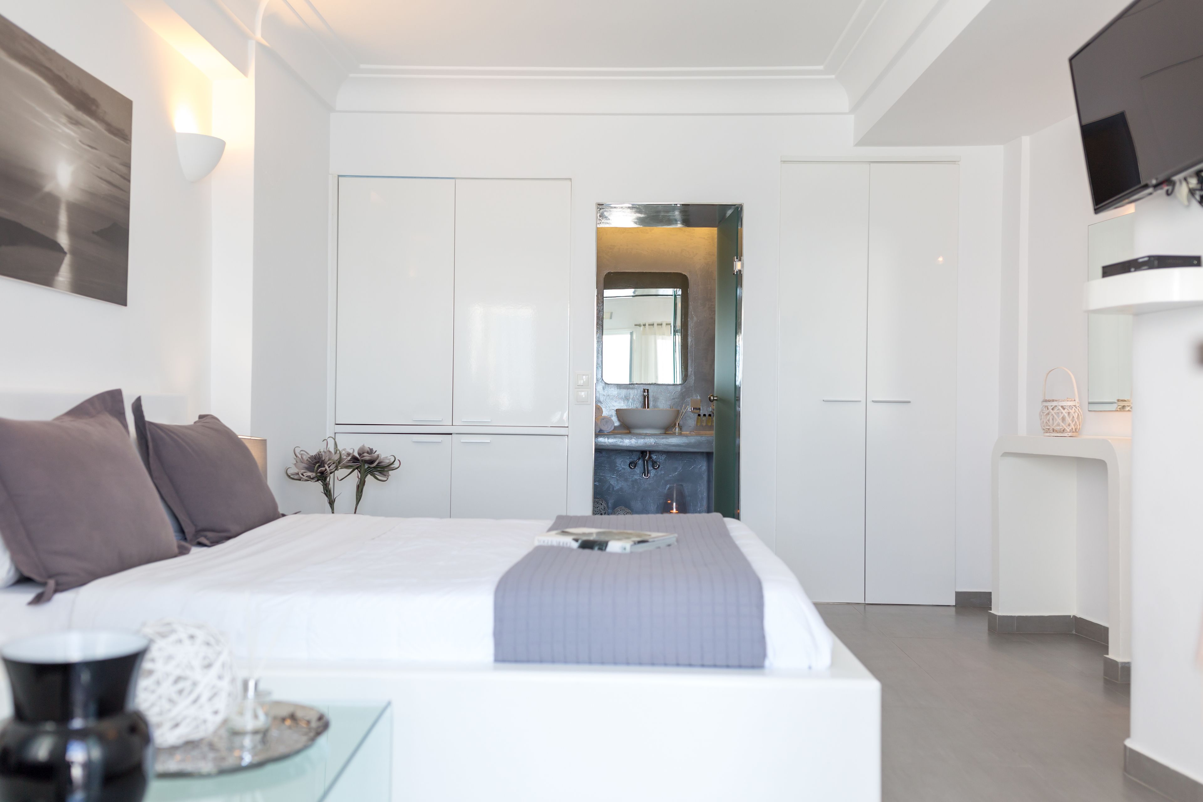 A modern bedroom with a large bed, a bedside table, a mirror, and a view into the bathroom.