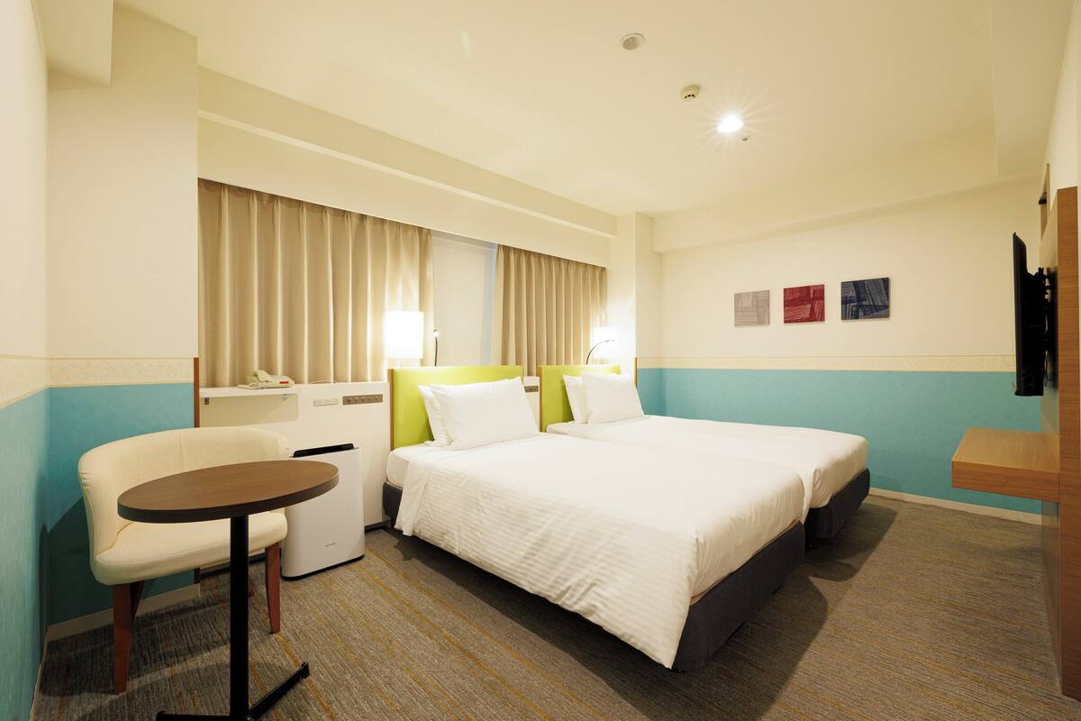 A hotel room with a bed, a chair, a desk, and a small table.