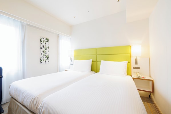 A hotel room with two beds, a green headboard, white bedding, a nightstand with a lamp, and a wall-mounted phone. - Holiday Inn Ana Sapporo Susukino by IHG (Sapporo)