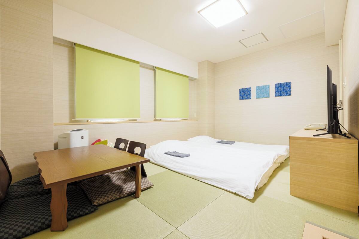 A hotel room with a bed, a desk, a chair, a television, and a window with blinds.