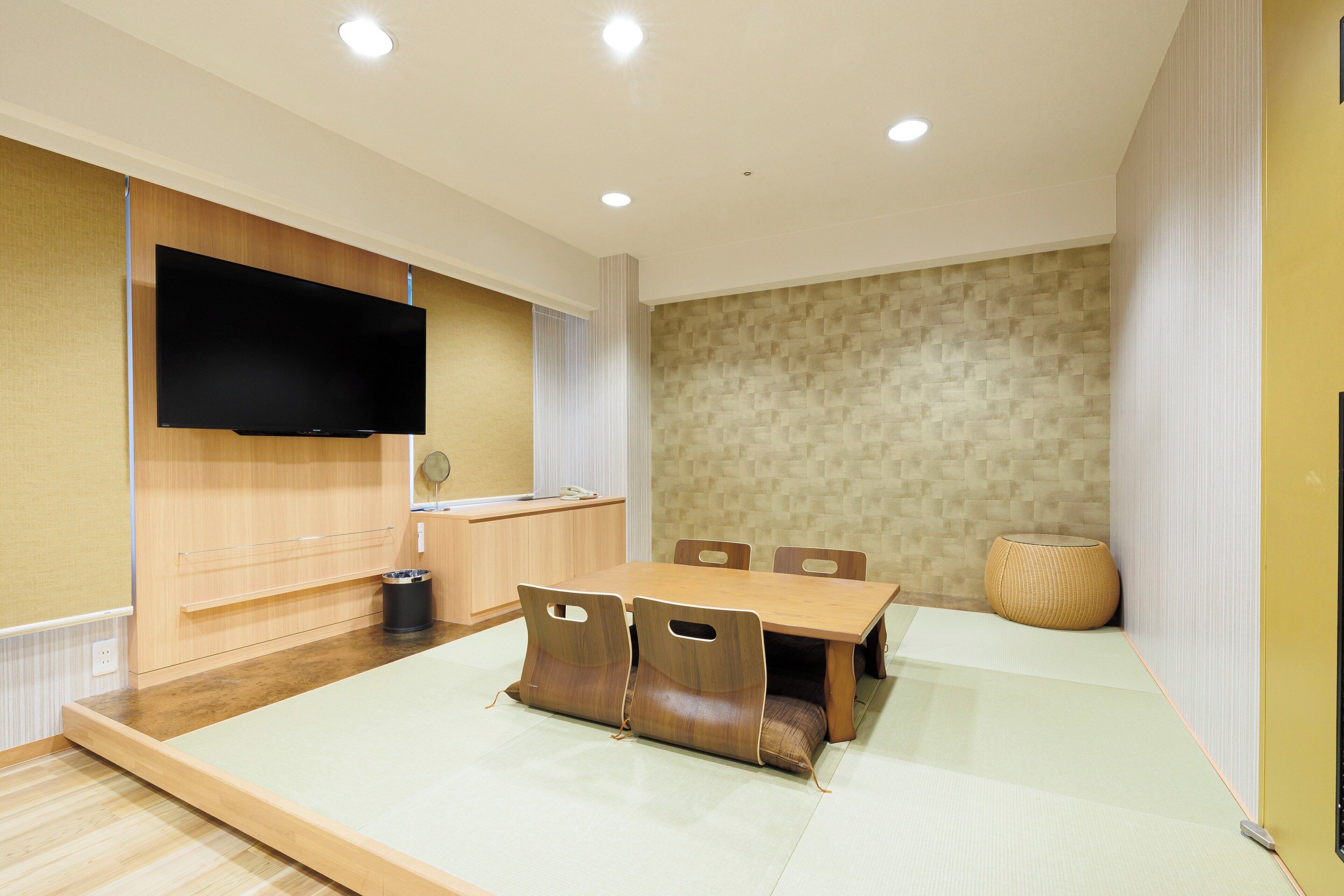 Un comedor moderno con una mesa y sillas de madera, un televisor de pantalla plana en la pared, y una zona de cocina con un lavamanos y encimera.