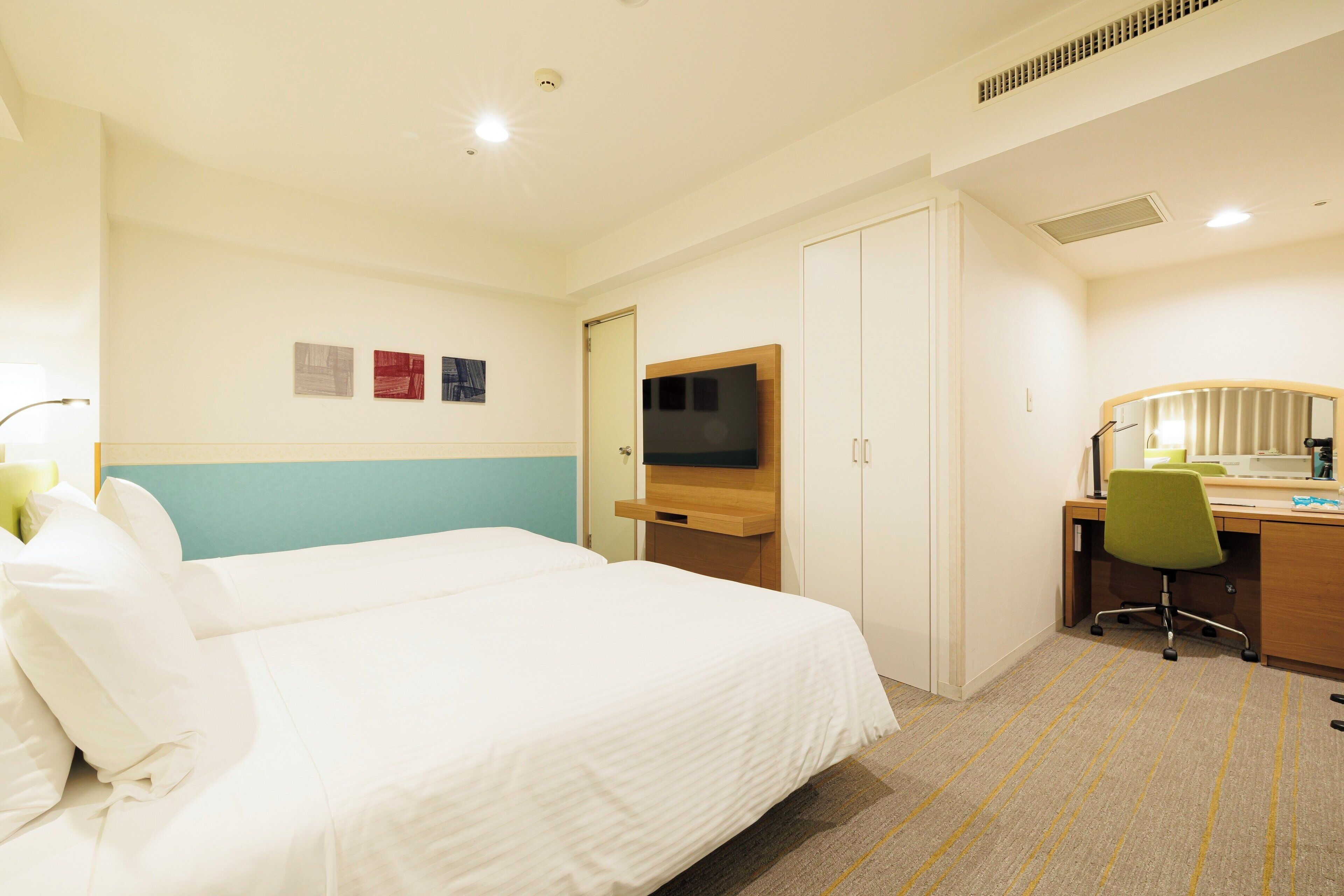 A hotel room with a bed, a desk, a chair, a TV, and a door.