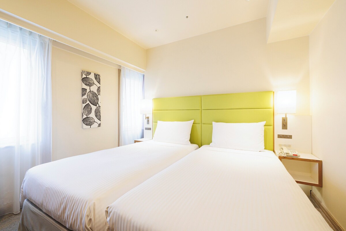 Une chambre d’hôtel avec deux lits, une tête de lit verte, une table de chevet avec une lampe et une œuvre d’art murale.
