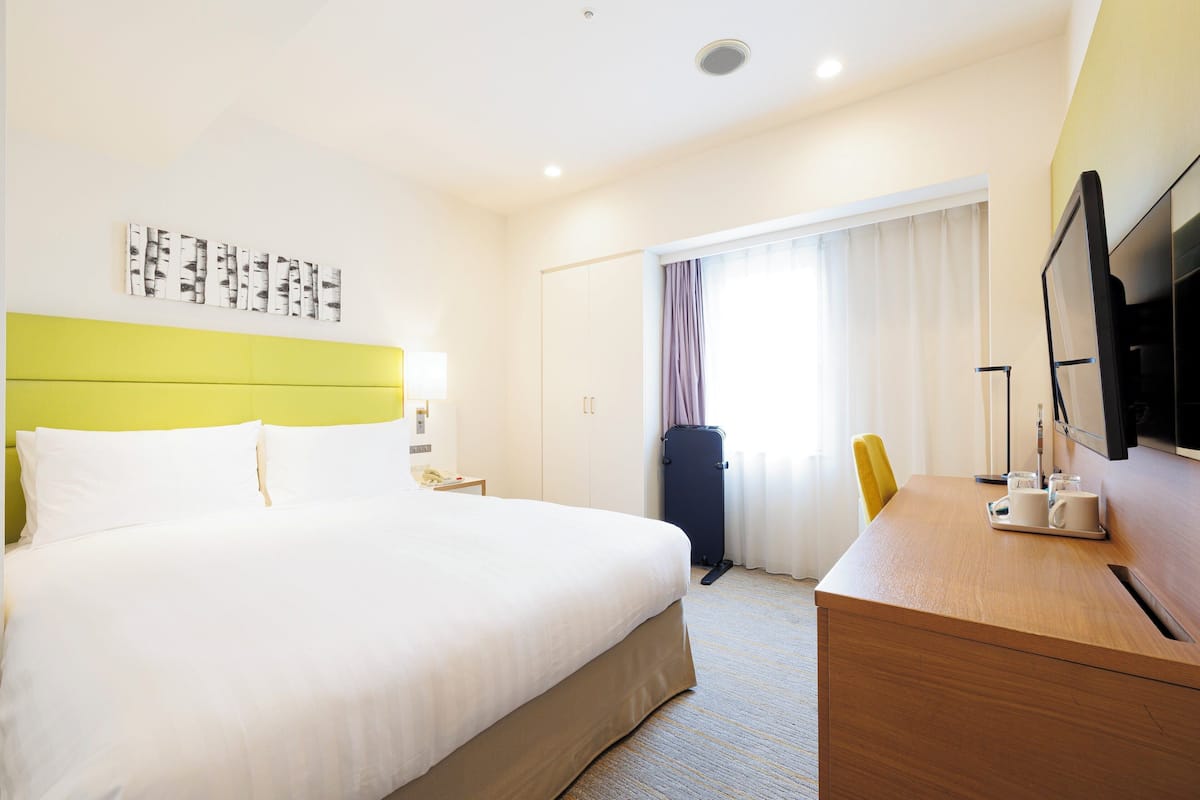 A hotel room with a large bed, a desk with a chair, a television, and a window with curtains.