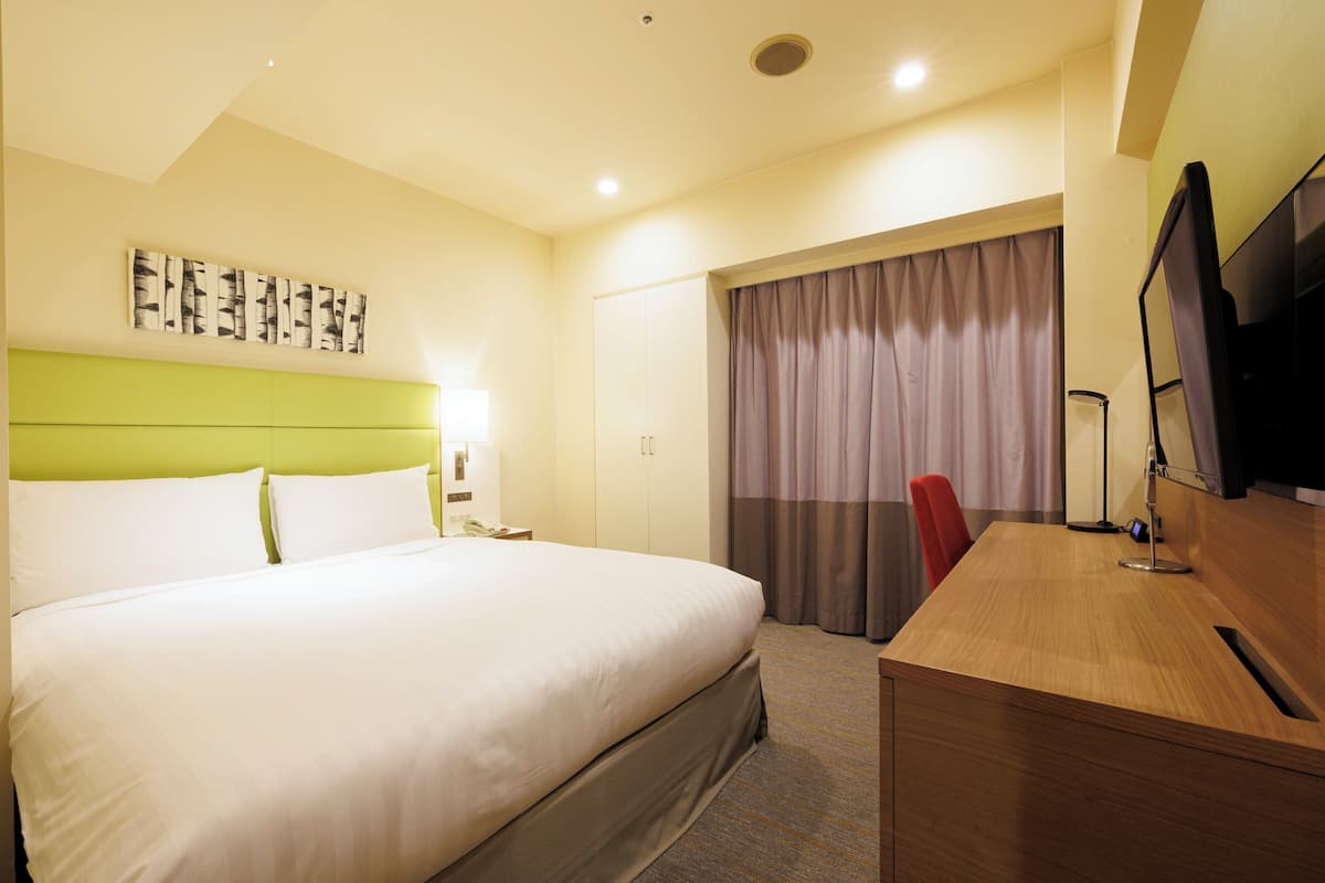 A hotel room with a bed, a desk, a television, and a window with curtains.