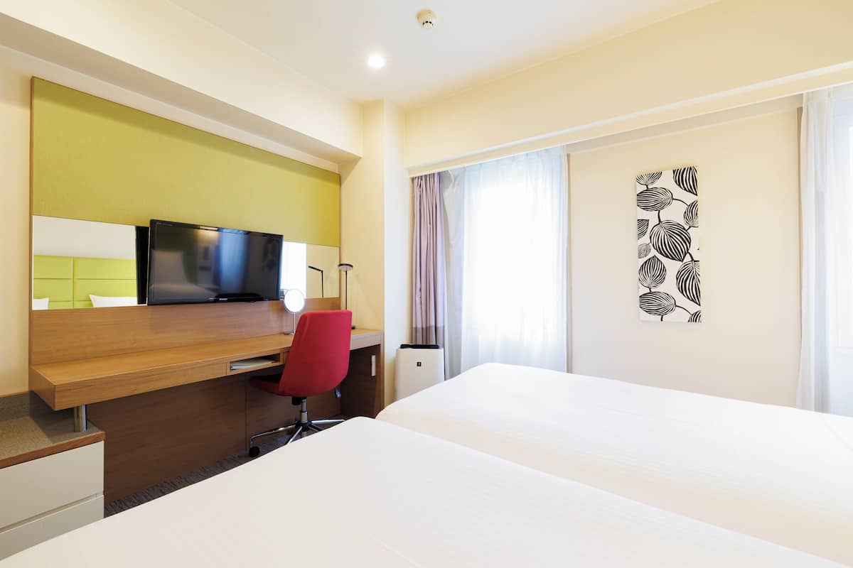 A hotel room with a bed, a desk with a computer, a red chair, and a television.