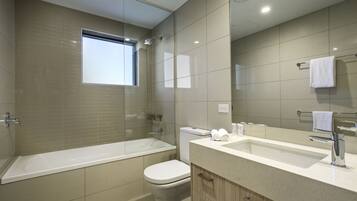A modern bathroom with a bathtub, toilet, and vanity with a sink and mirror.
