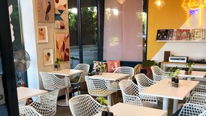 A modern cafe with white lattice chairs and tables, artwork on the walls, and a neon sign. - Quest Woolloongabba (Woolloongabba)