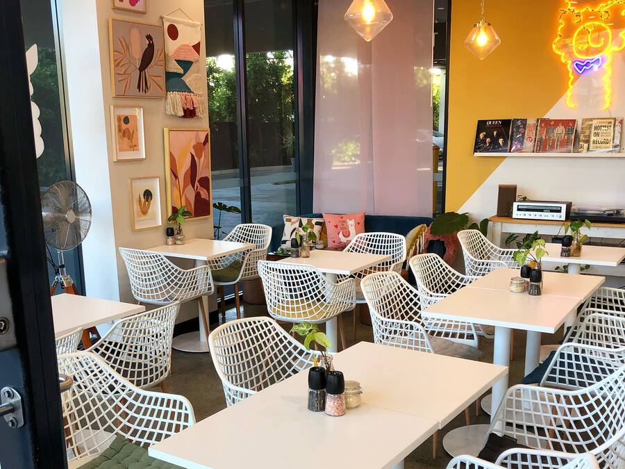 Un café moderno con sillas y mesas de celosía blanca, obras de arte en las paredes y un letrero de neón.