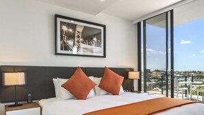 A modern hotel room with a large bed, two bedside tables with lamps, a framed picture on the wall, and a large window offering a city view. - Quest Woolloongabba (Woolloongabba)