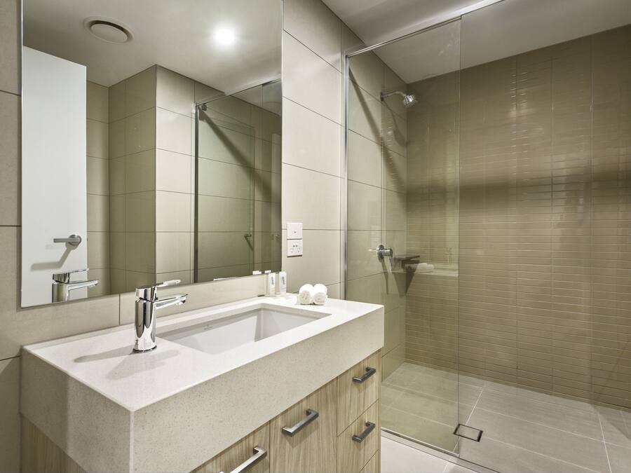Un baño moderno con ducha envuelta en vidrio, un espejo grande y un lavabo con cajones de almacenamiento.