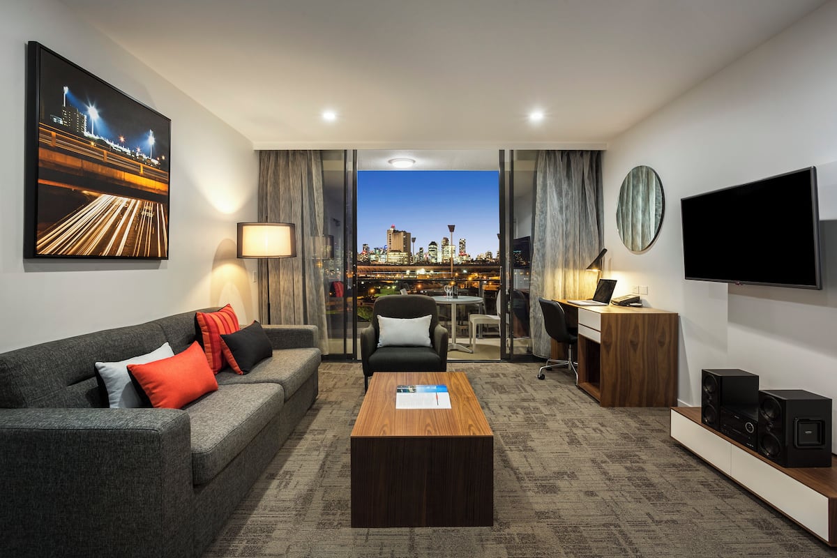 Une chambre d’hôtel moderne avec vue sur la ville, comprenant un canapé, une table basse, un bureau et un téléviseur.
