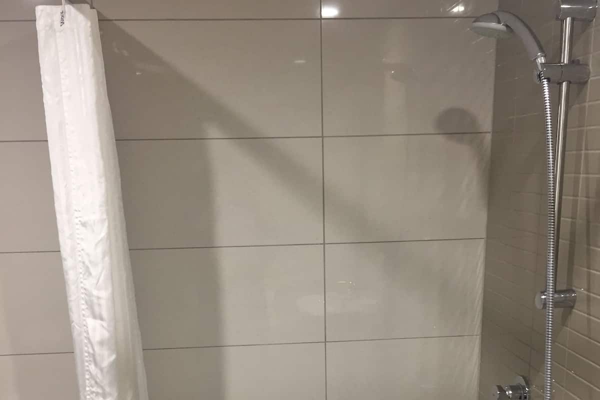 Une cabine de douche avec un pommeau de douche blanc, un flexible de douche et un siège de douche blanc.