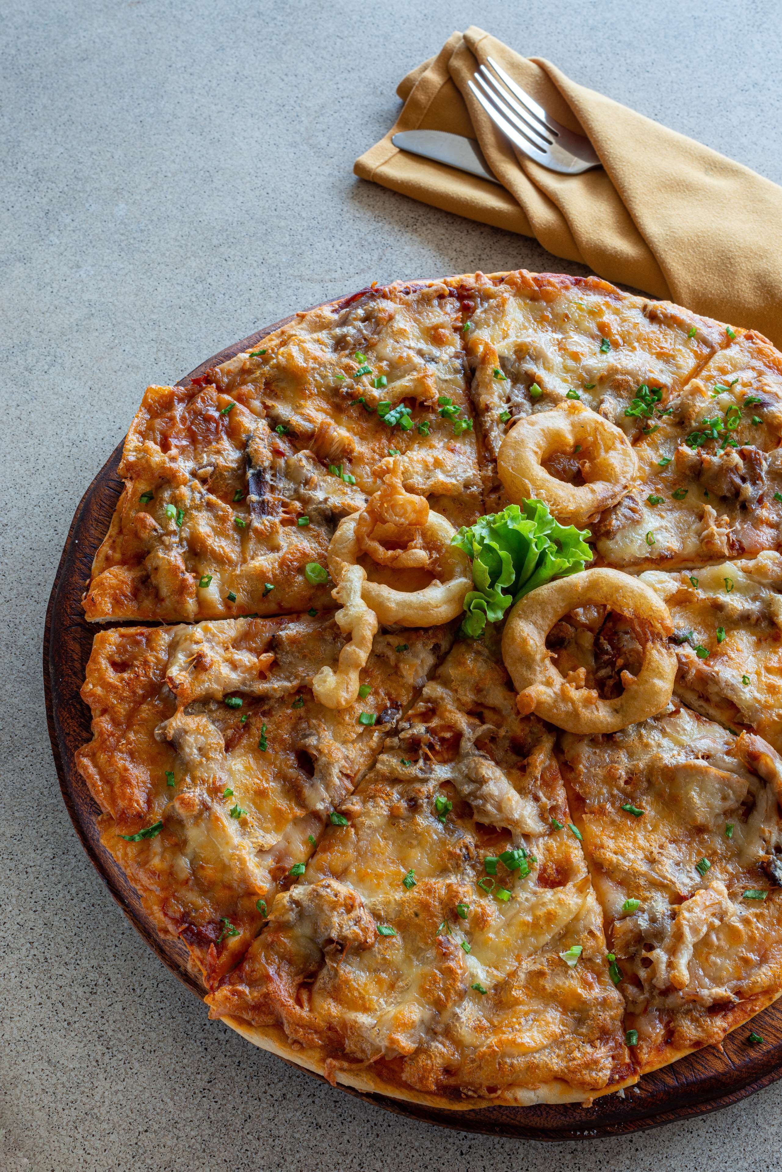 A pizza with toppings and onion rings on a wooden board.