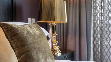 A neatly made bed with a large, plush pillow, a decorative lamp, and a dark nightstand.