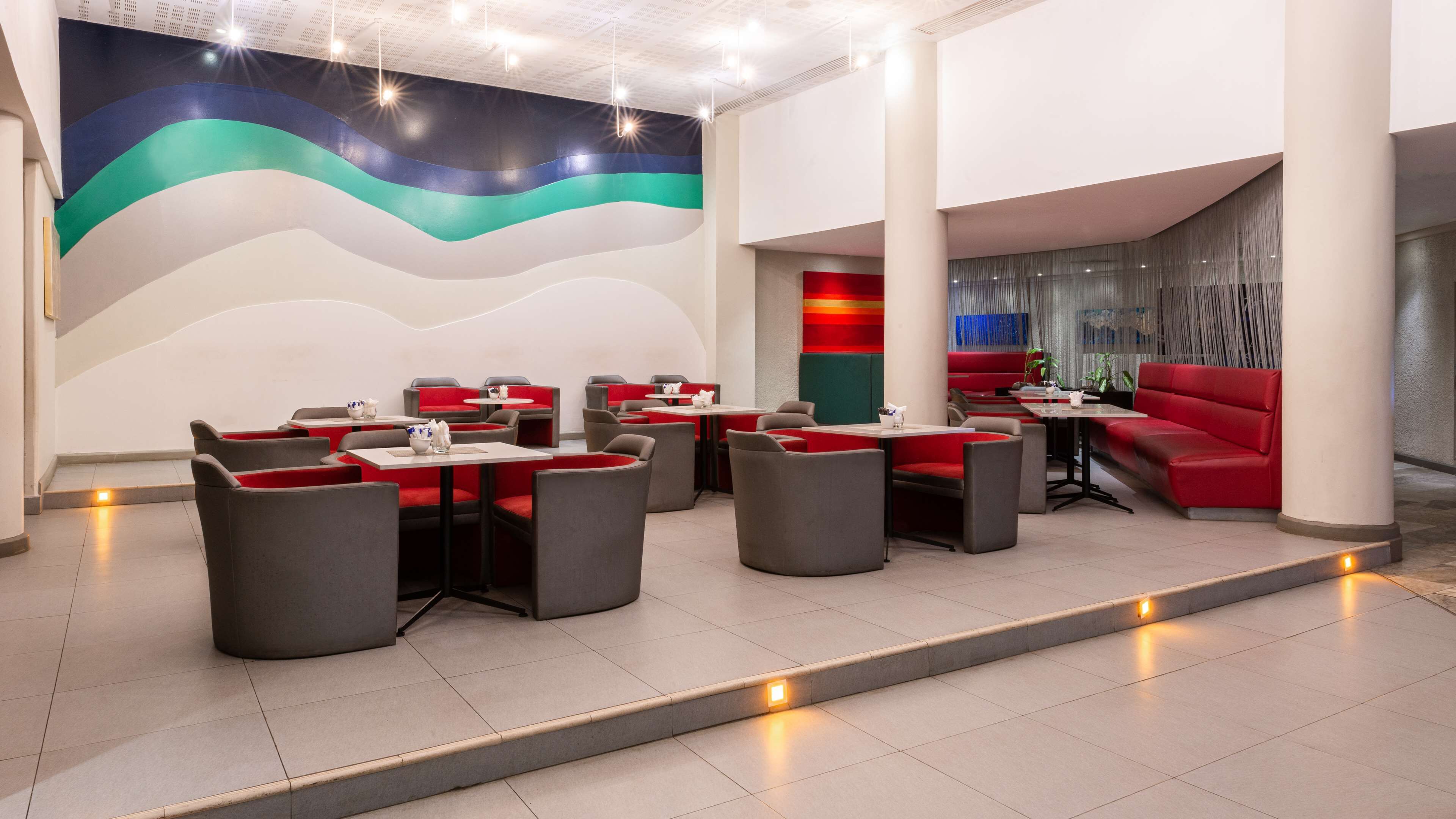 Un restaurant moderne avec des sièges rouges et gris, une fresque murale colorée et un mur d’accent rouge.
