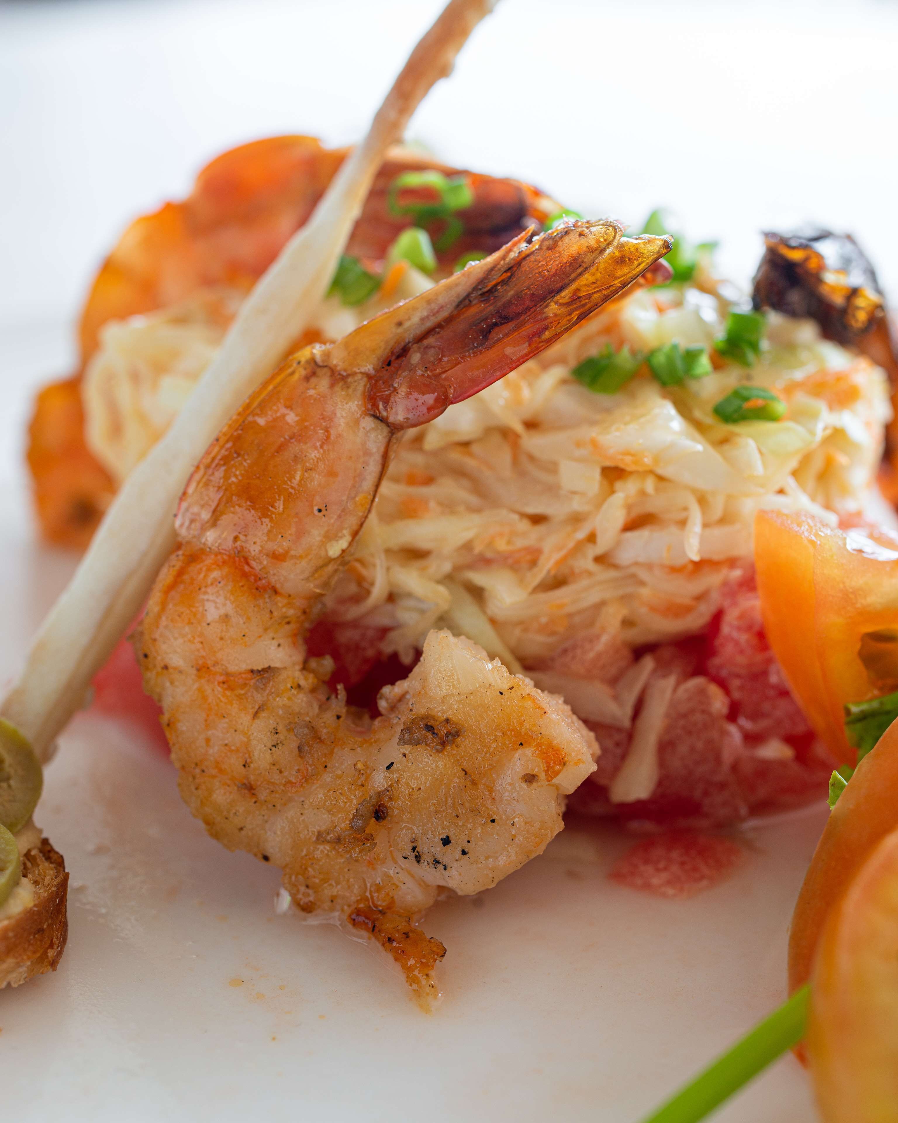 Primer plano de un plato de mariscos con camarones, posiblemente ensartados, adornado con hierbas.