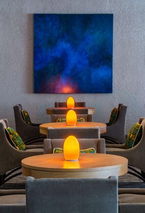 Un espace de détente moderne avec une table ronde en bois, des fauteuils à revêtement gris et un grand tableau abstrait accroché au mur.