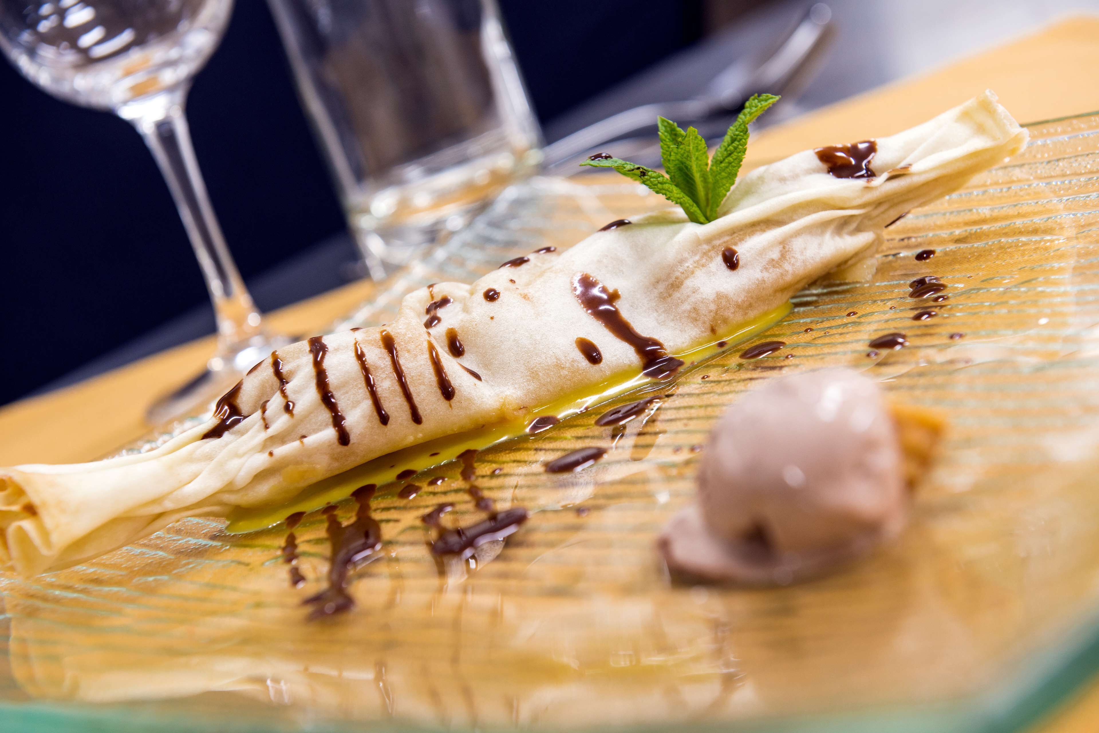 A dessert on a glass plate with chocolate drizzle and mint garnish.