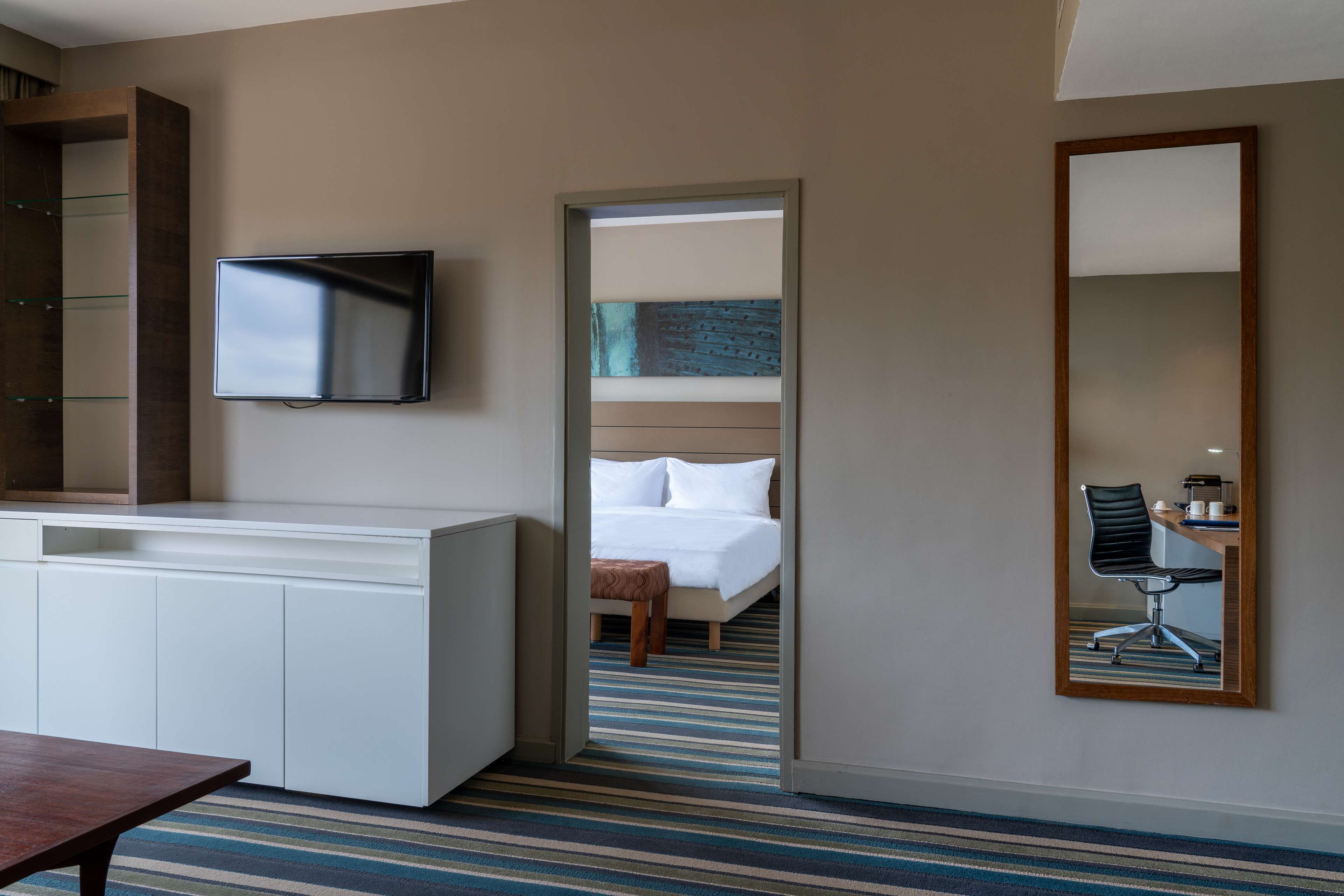 A hotel room with a bed, a desk with a chair, a television, and a mirror.