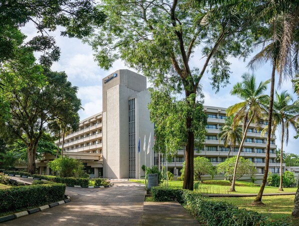 Un hôtel moderne doté d’une tour centrale, entouré d’une végétation luxuriante et de palmiers.
