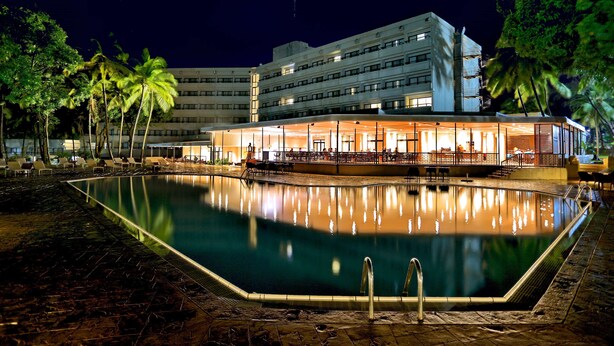 Un hotel con piscina, palmeras y una fachada iluminada durante la noche.
