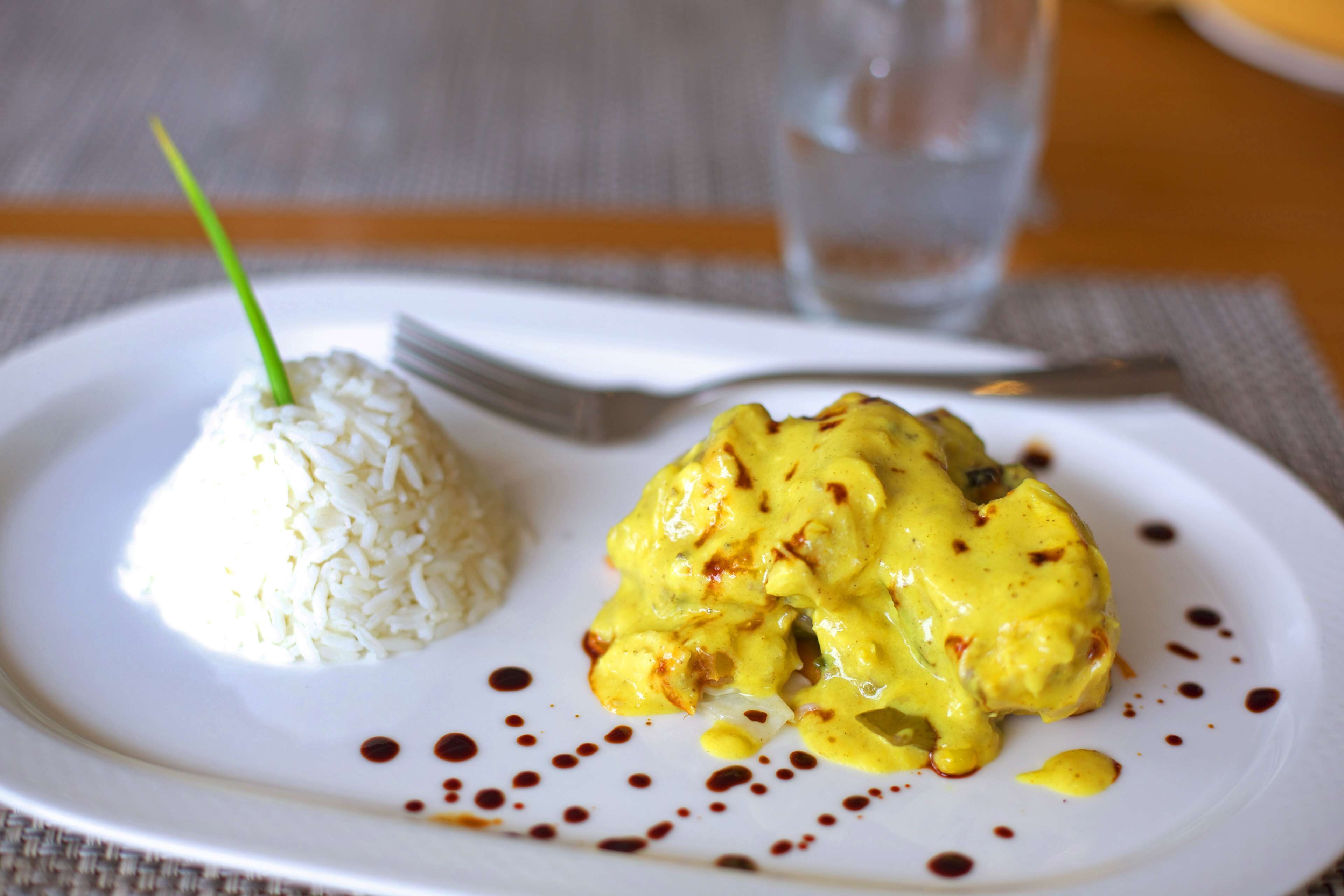 A plate with white rice and a yellow curry dish, garnished with a green chive and dark sauce.