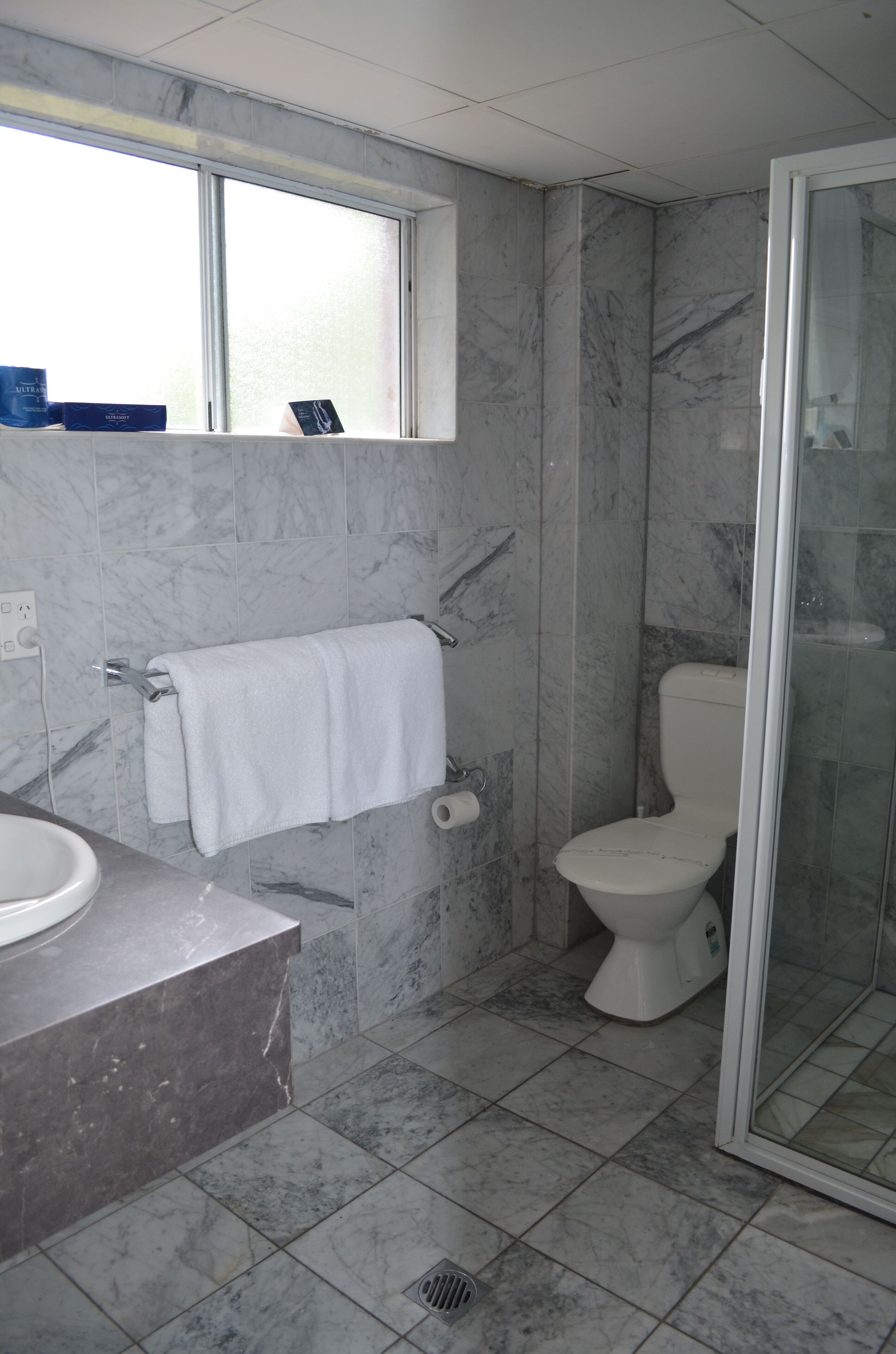 A bathroom with a marble floor, a white sink, a toilet, and a glass shower enclosure.