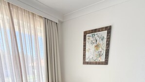 Une pièce comprenant deux fauteuils en cuir, une petite table ronde, une œuvre d’art florale encadrée et des rideaux en voile léger.