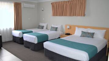Quarto de hotel com três camas, cada uma com colcha branca e azul-turquesa, e uma janela grande com cortinas.