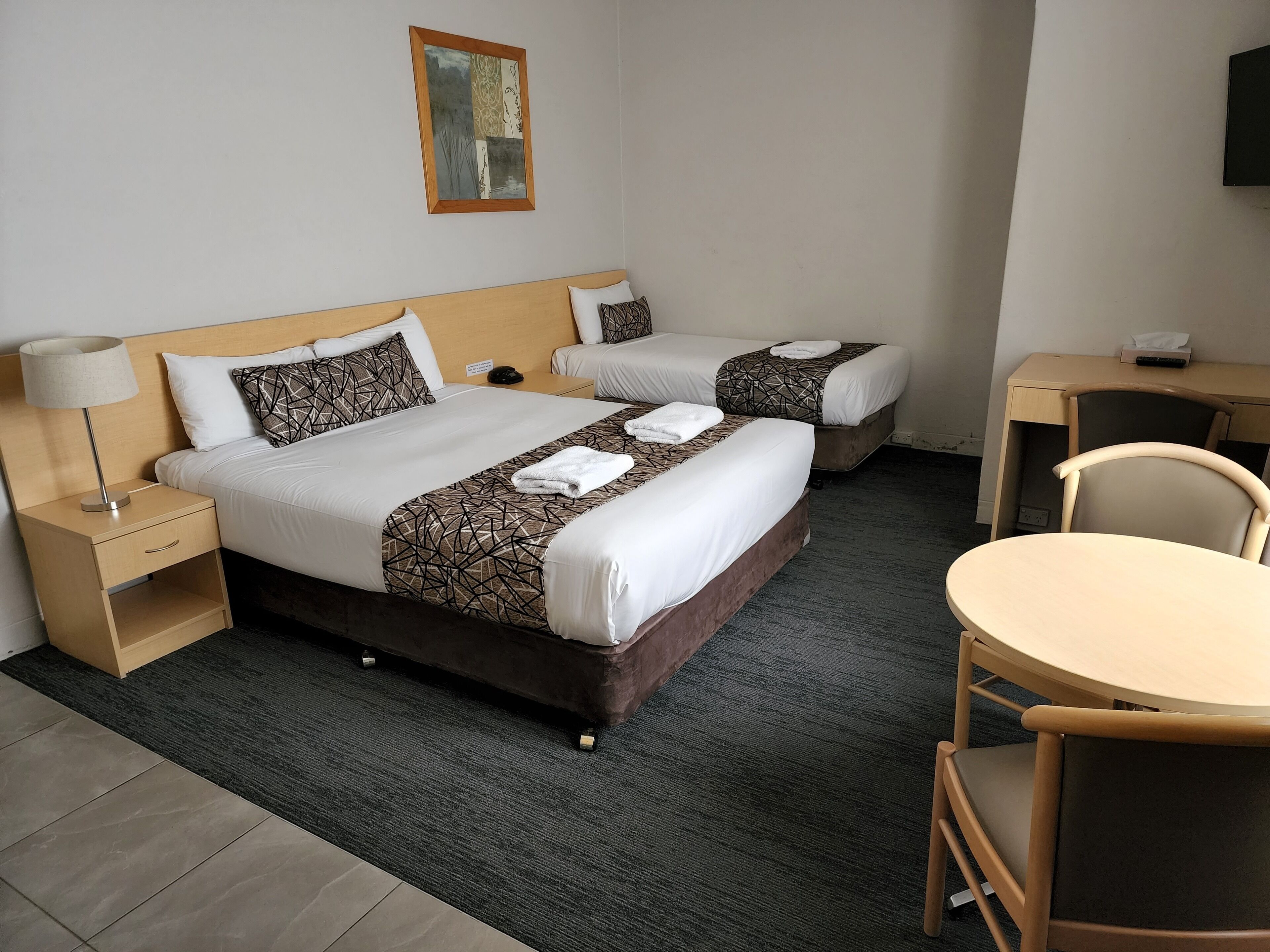 Ein Hotelzimmer mit zwei Betten, einem Schreibtisch, einem Stuhl und einer Lampe.