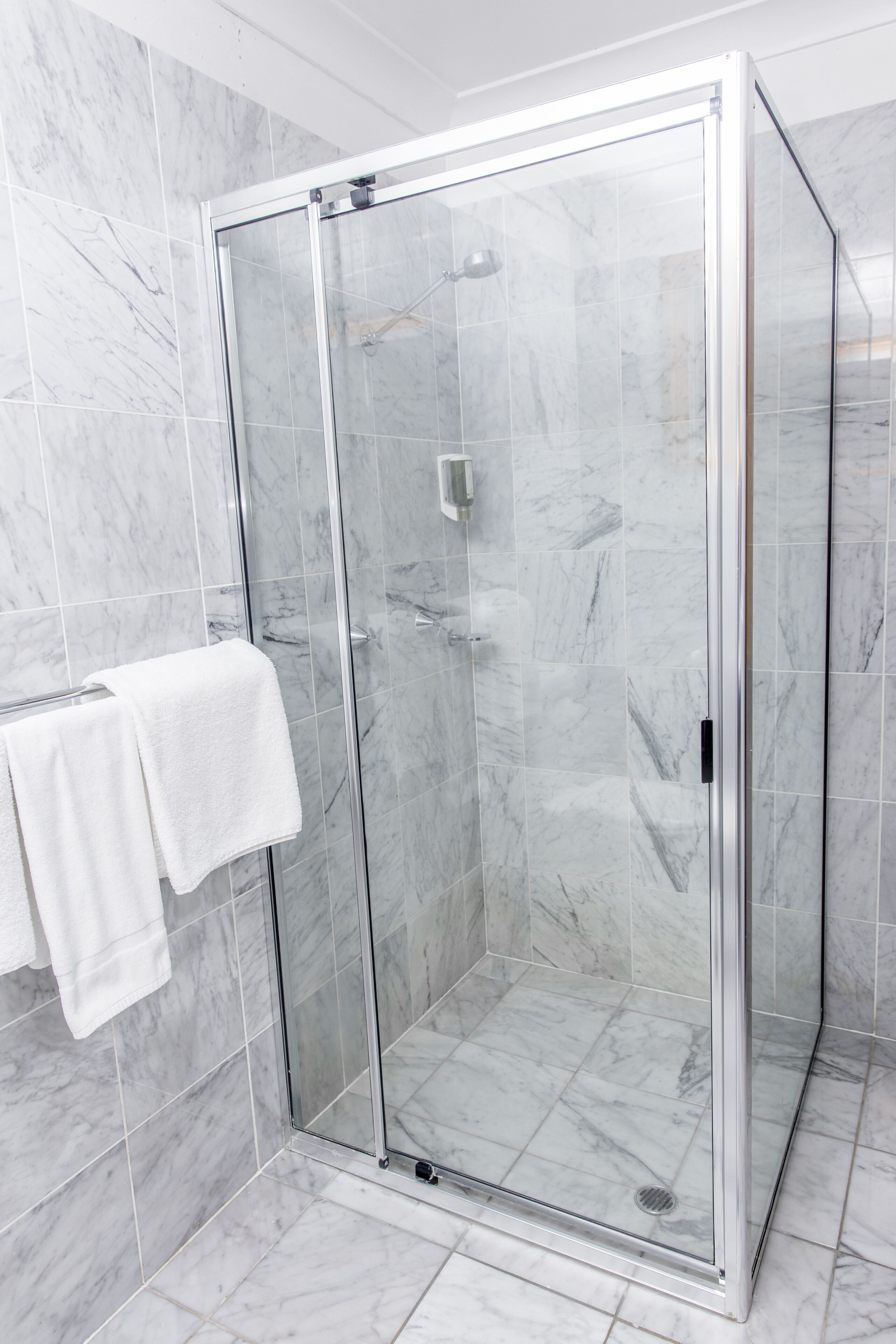 A glass-enclosed shower stall with a white towel hanging on a rack to the left.