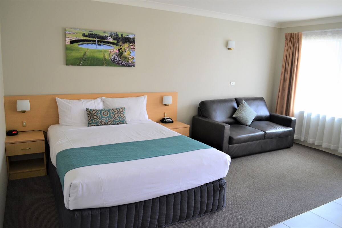 Habitación de hotel con una cama grande, un sofá de cuero, un cuadro en la pared y una ventana con cortinas.