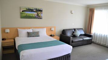 A hotel room with a large bed, a leather sofa, a painting on the wall, and a window with curtains.