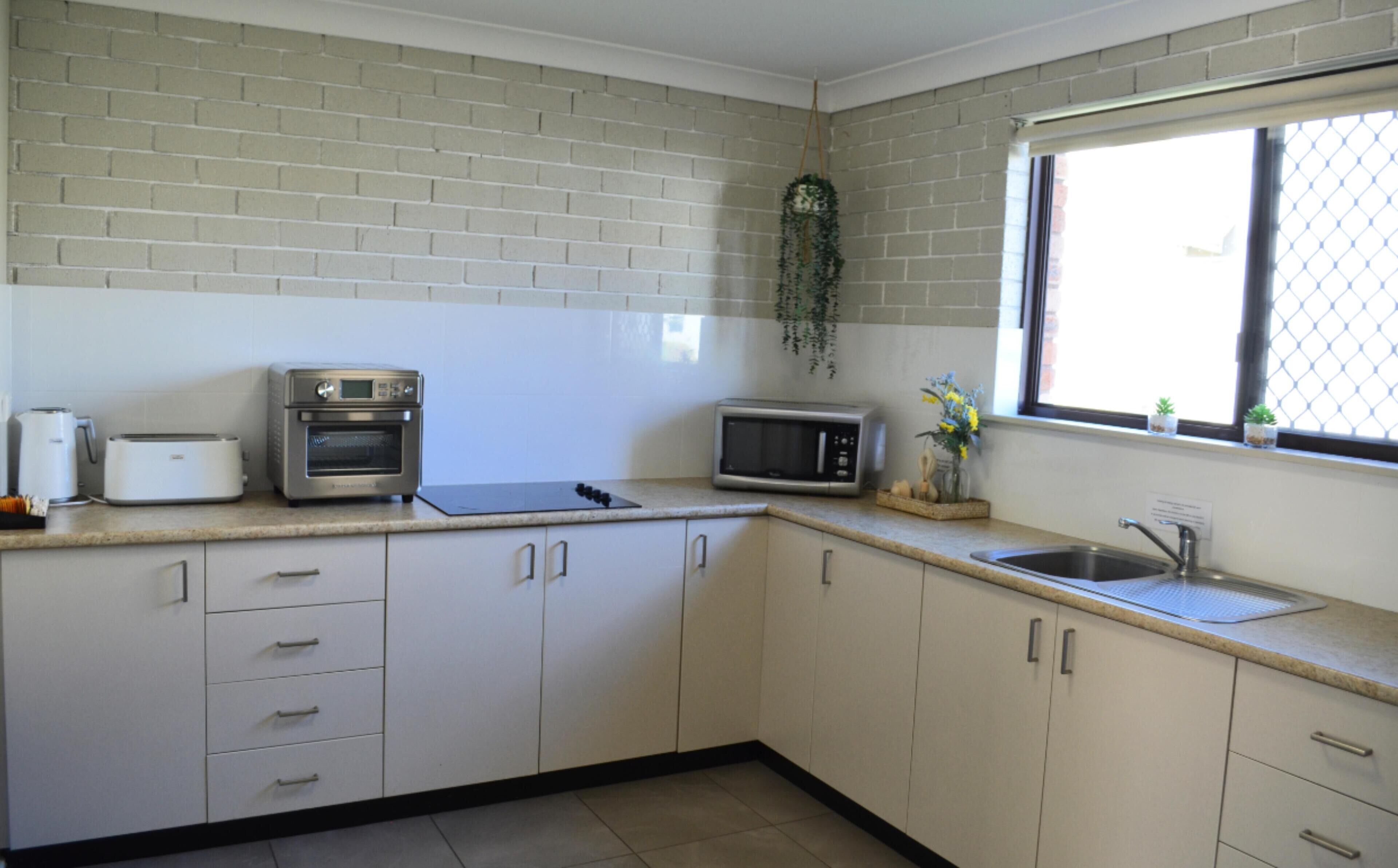A kitchen with white cabinets, a toaster, an oven, a microwave, and a sink.