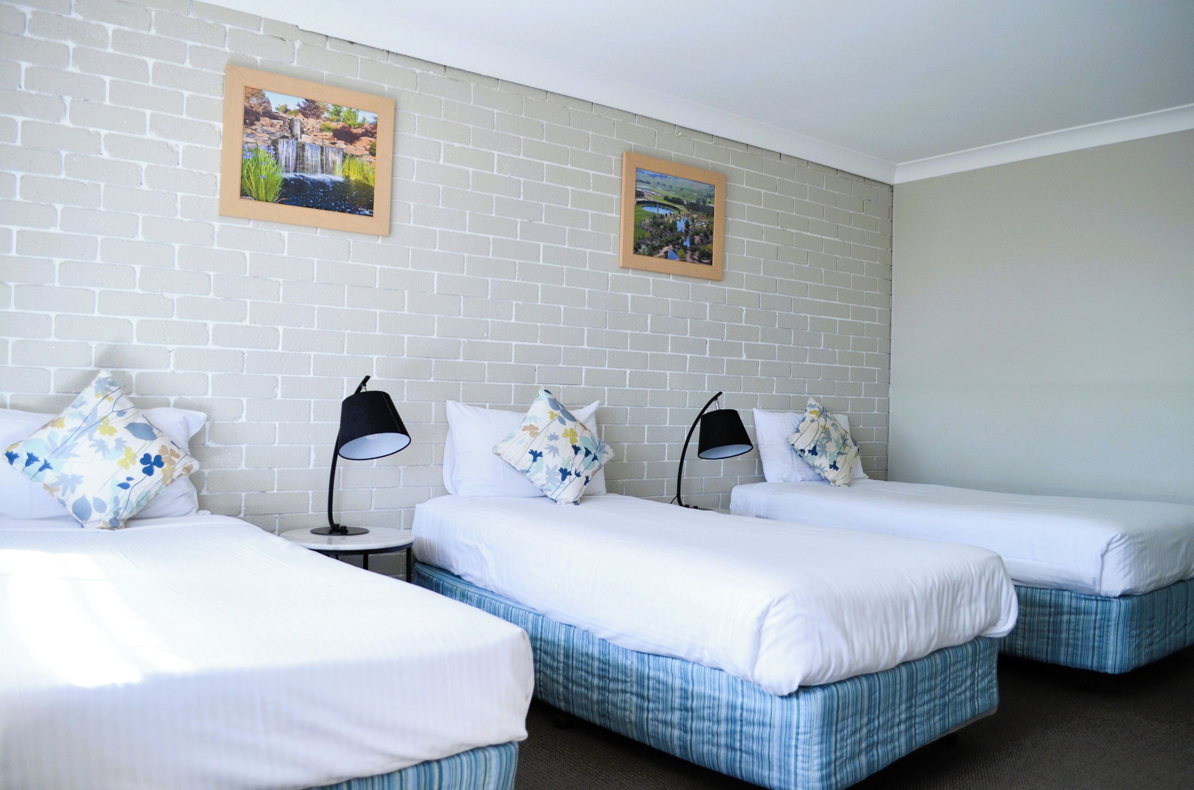 Habitación de hotel con tres camas individuales, ropa de cama blanca y dos lámparas negras.
