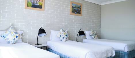 Habitación de hotel con tres camas individuales, ropa de cama blanca y dos lámparas negras.