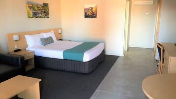 A hotel room with a bed, a desk, a chair, and two paintings on the wall.