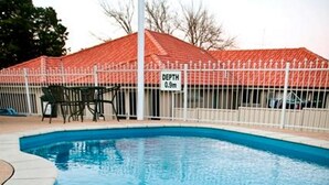 Une piscine dont la profondeur est indiquée à 0,9 mètre, entourée d’une clôture blanche et bordée d’un bâtiment au toit rouge.