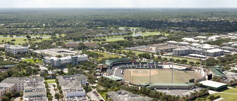 An aerial view of a stadium with a baseball field, surrounded by residential buildings and greenery.