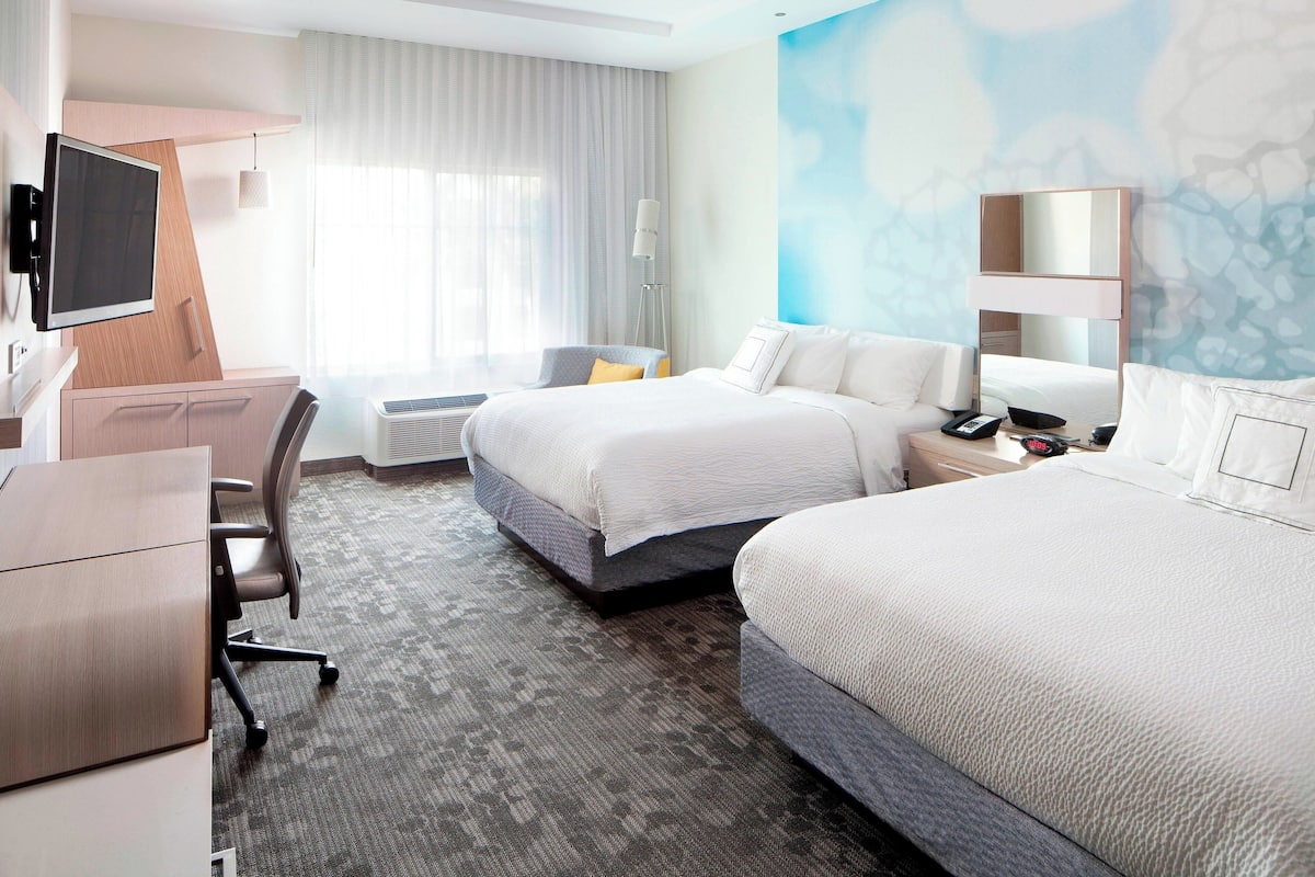 A hotel room with a bed, a desk, a chair, a TV, and a large window with curtains.