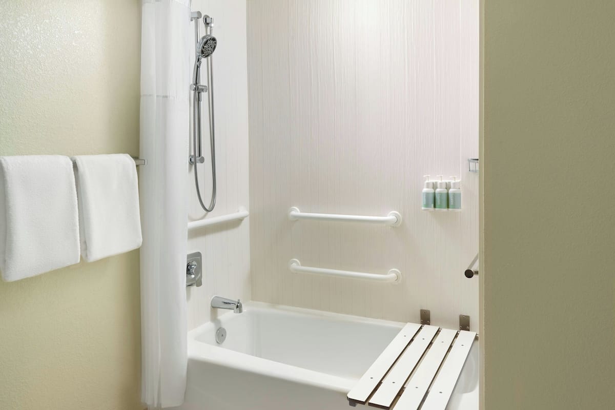 A bathroom with a bathtub, a shower, and handrails.