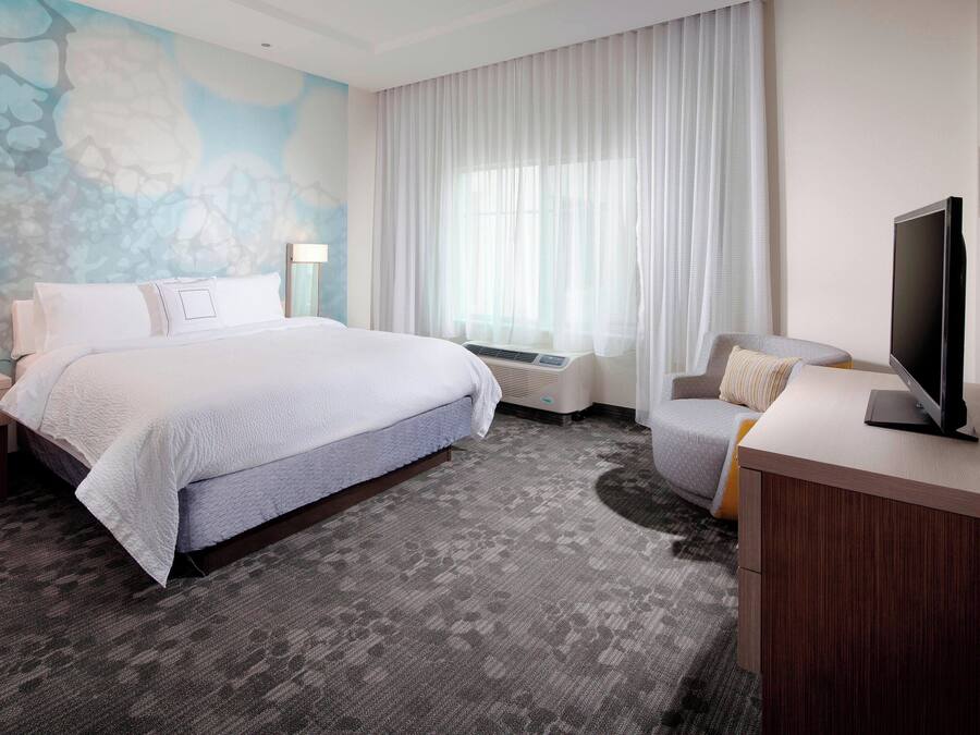Habitación de hotel con una cama grande, un escritorio con televisor de pantalla plana, una silla, una mesita de noche y una pared con un mural texturizado.