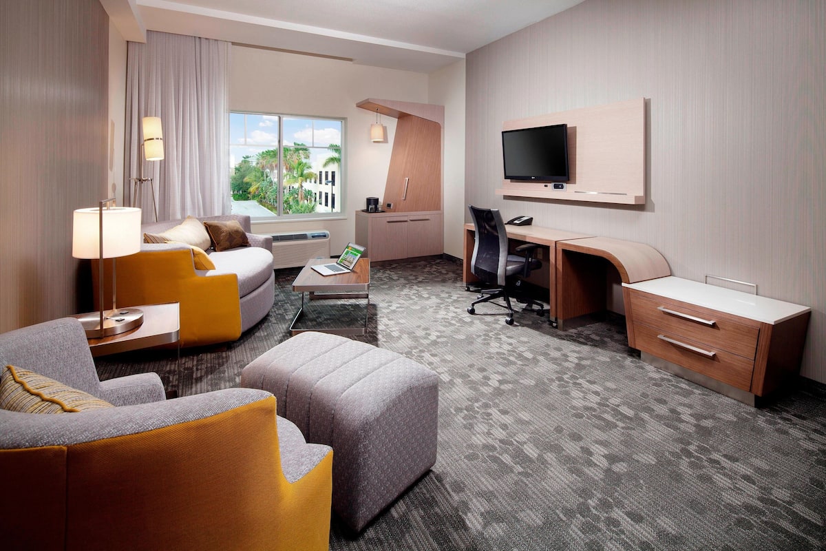A hotel room with a sofa, armchair, desk, and TV.
