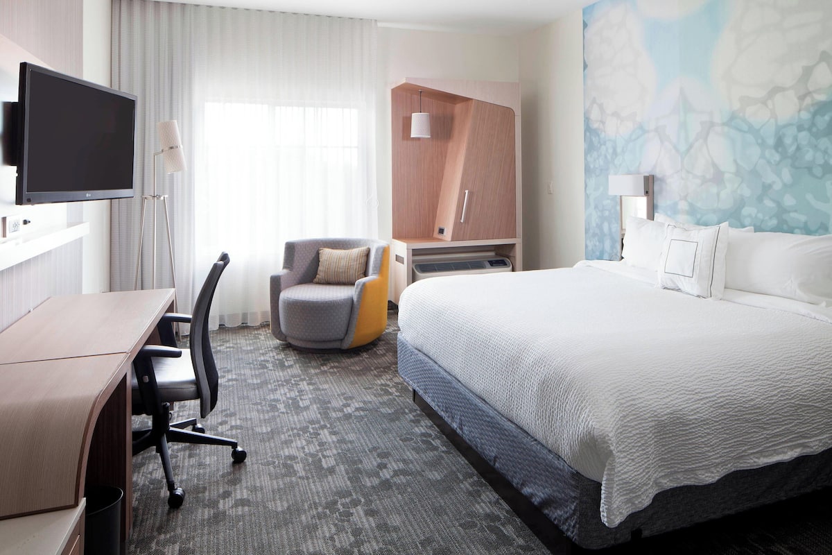 A hotel room with a bed, a desk, a chair, a wardrobe, and a television.