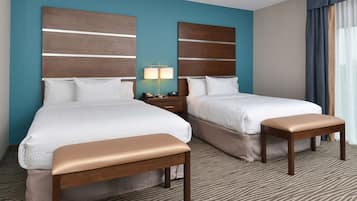 A hotel room with two beds, a bench, a nightstand with a lamp, and a view of the outdoors.
