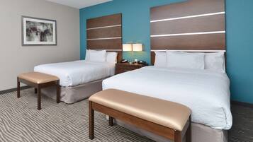 A hotel room with two beds, a bench, a nightstand with a lamp, and a framed picture on the wall.
